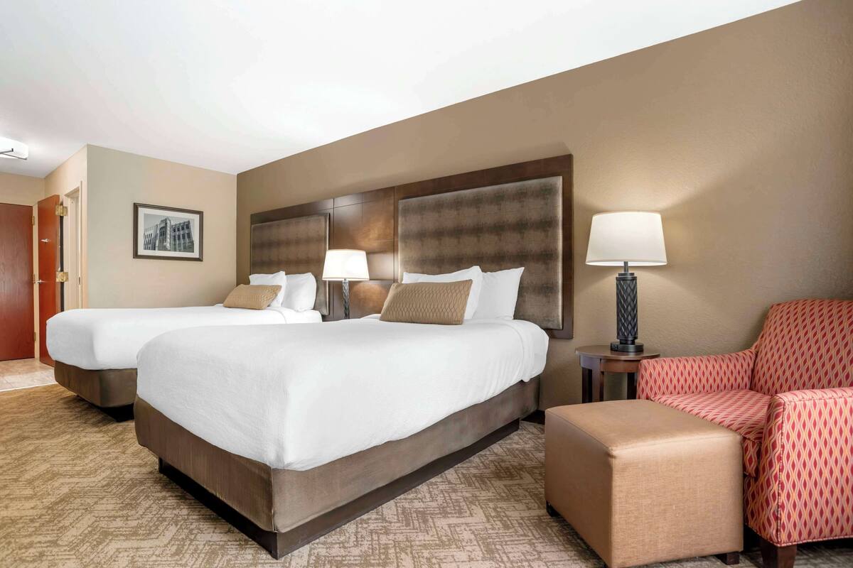 A hotel room with two beds, a sofa, a chair, and a lamp.