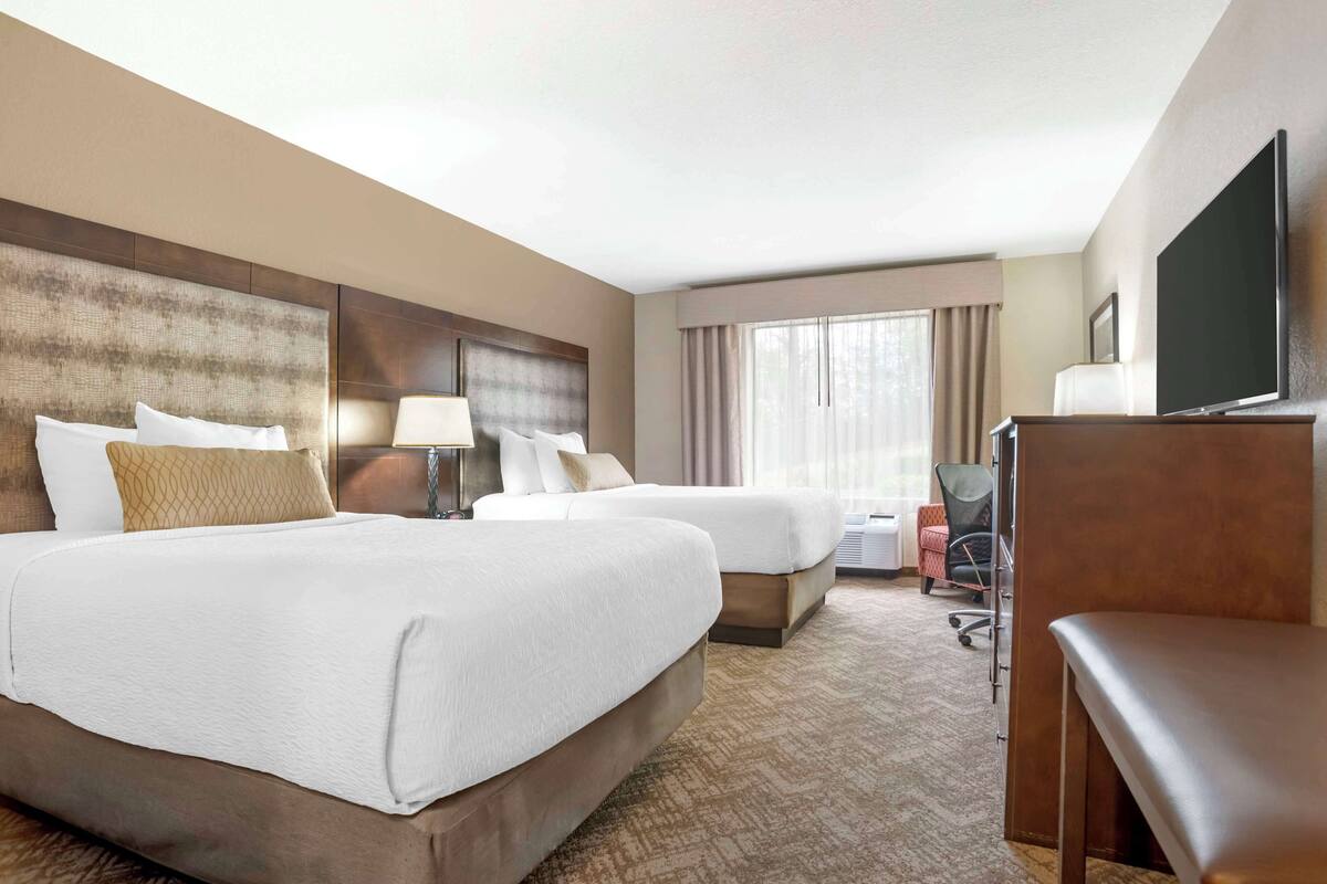 A hotel room with two beds, a desk, a chair, a TV, and a large window.