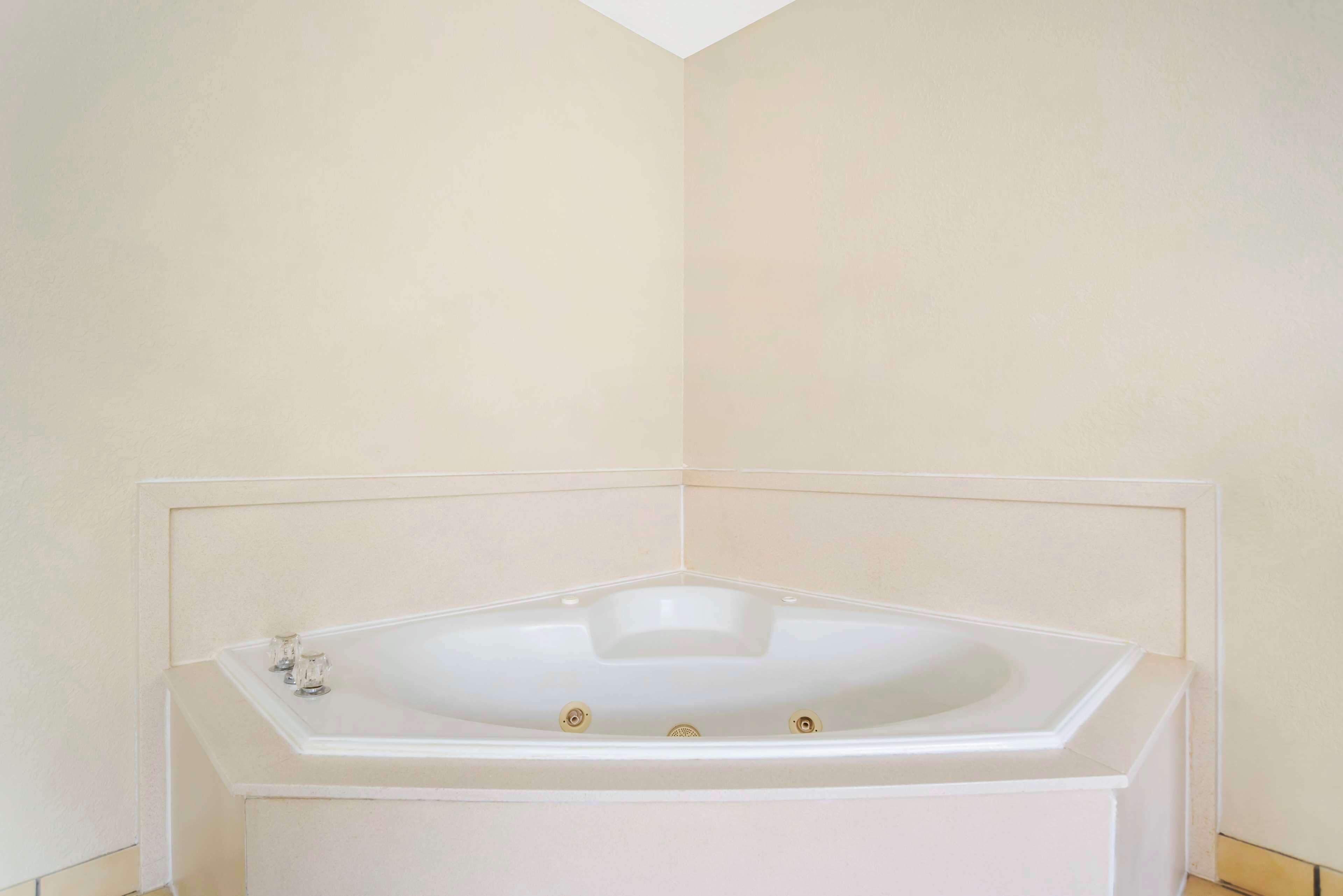 Una bañera de esquina con revestimiento blanco, asiento integrado y dos llaves.