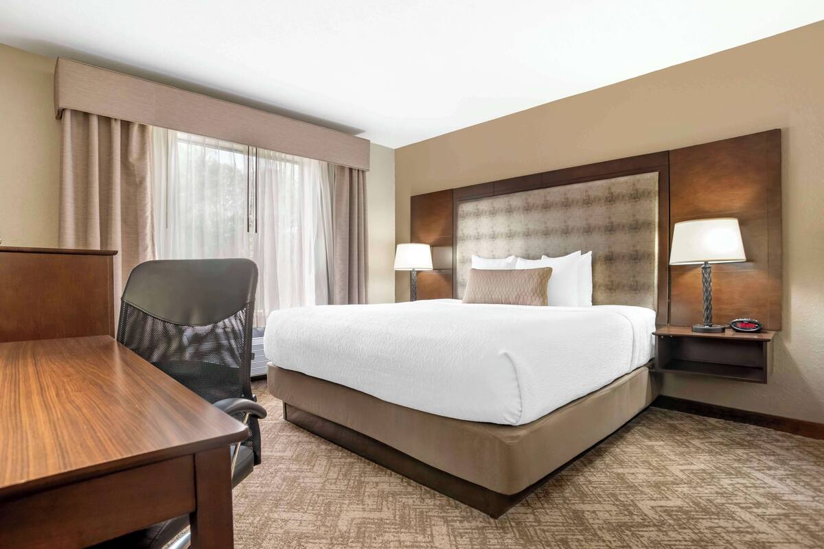 A hotel room with a large bed, a desk, a chair, and two bedside lamps.