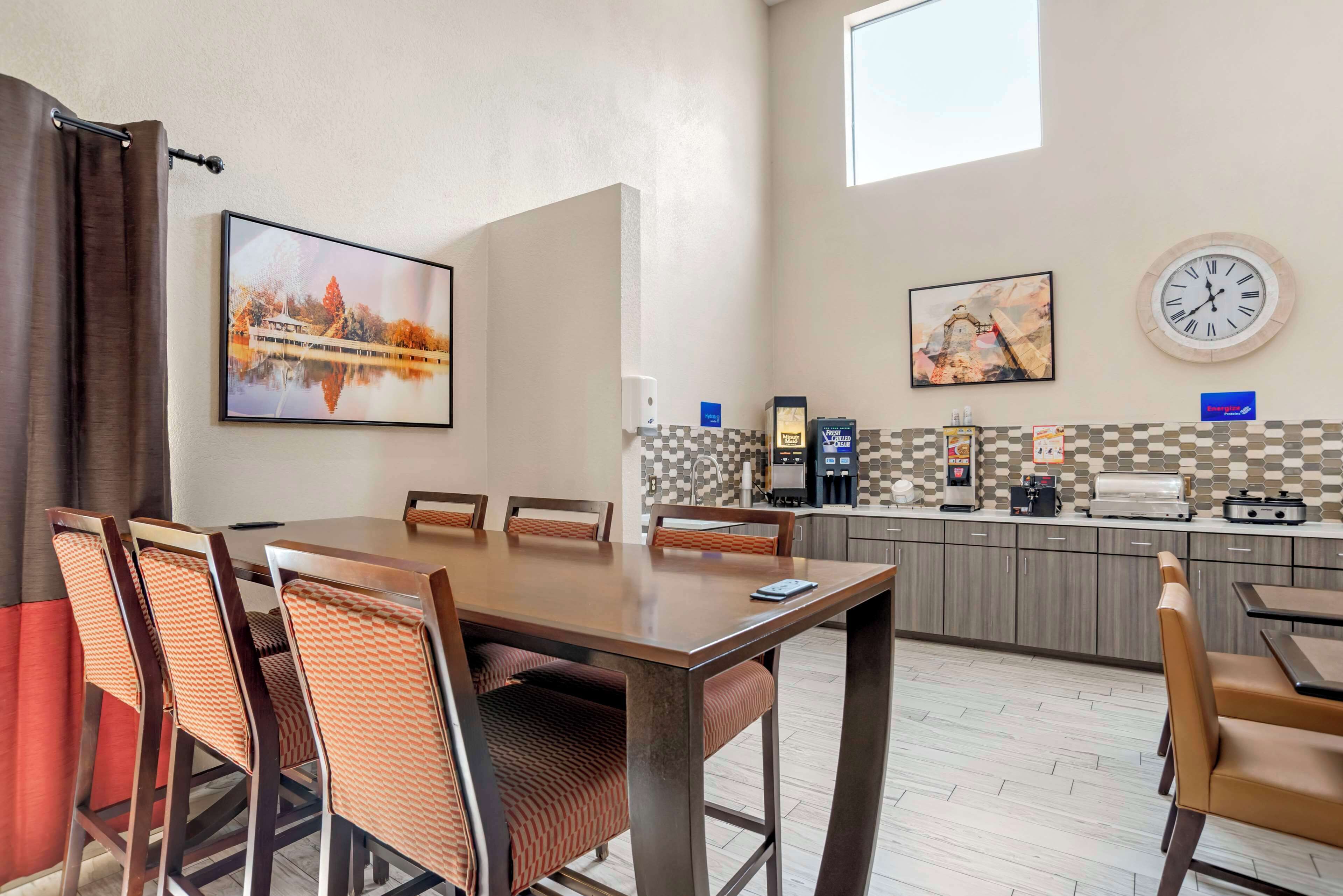 A dining area with a wooden table and chairs, a kitchen with a coffee machine, and artwork on the walls.