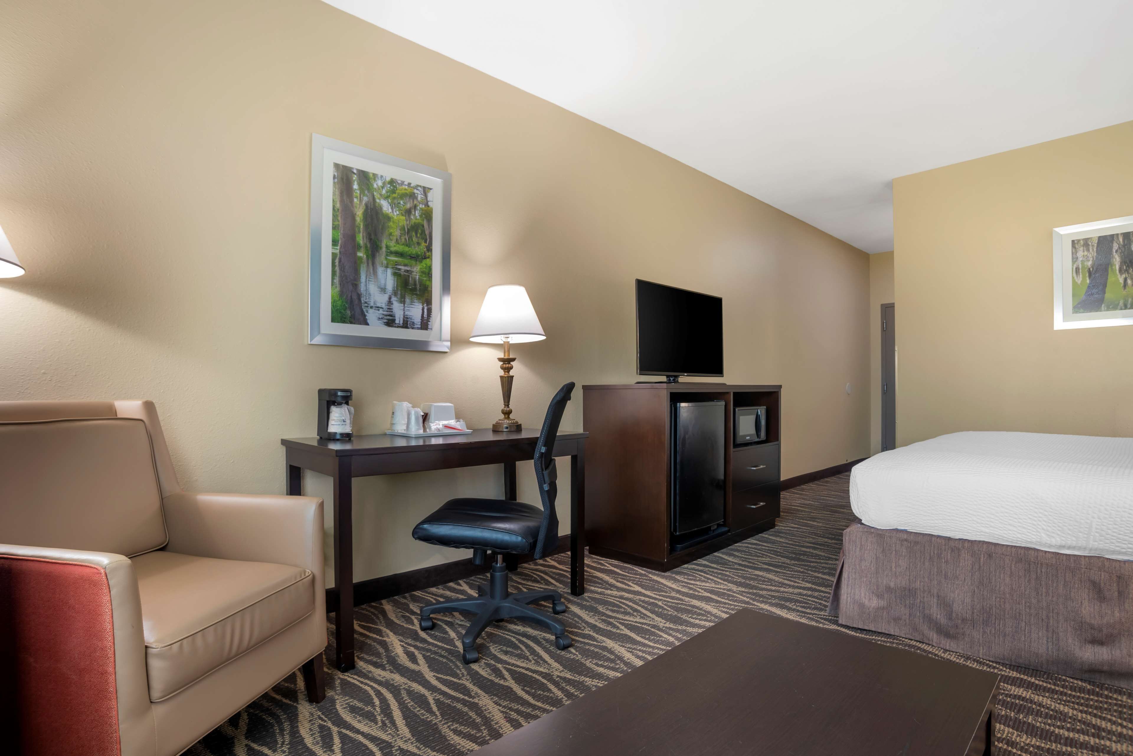 Una habitación de hotel con cama, escritorio con silla, televisor y cafetera.