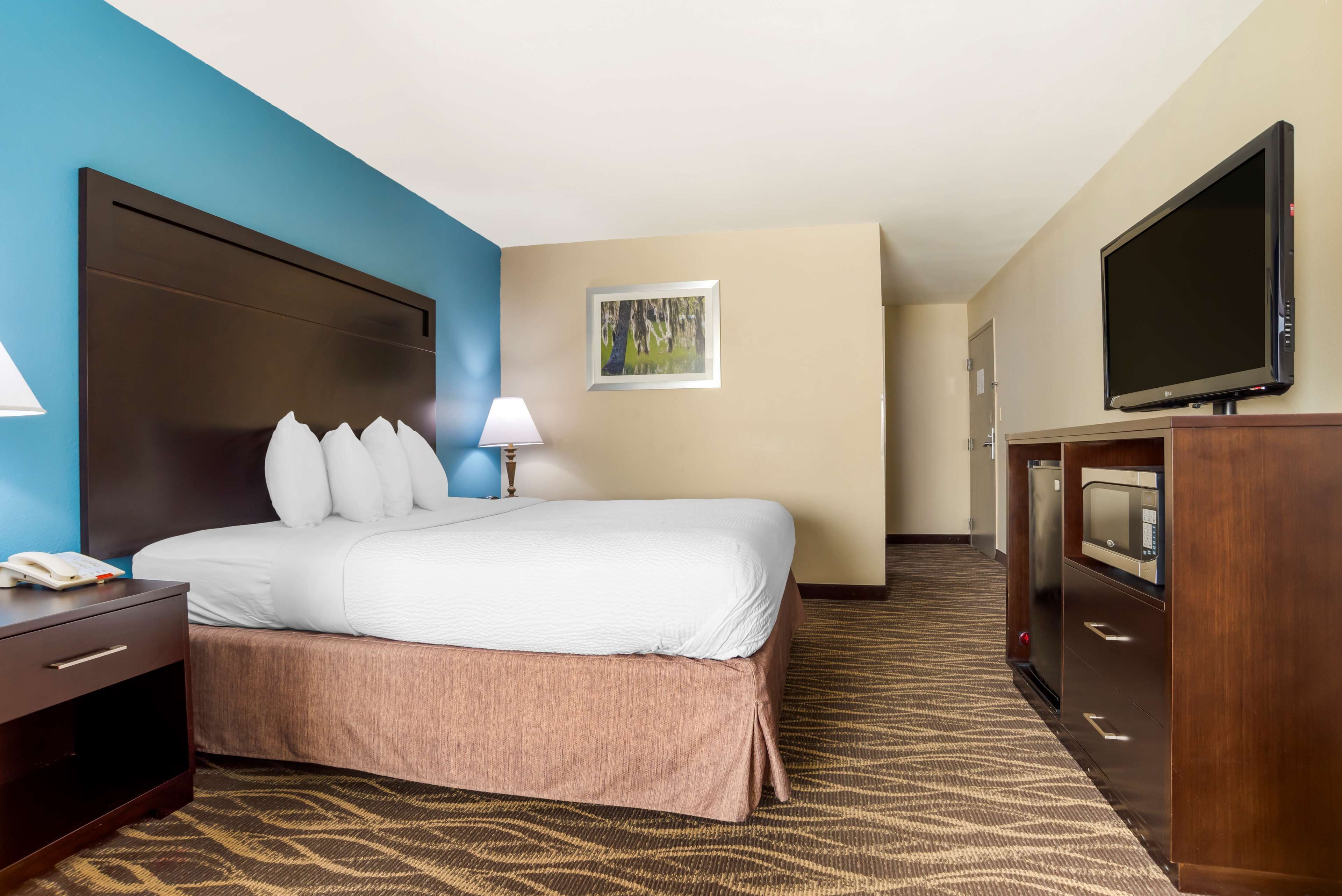 A hotel room with a large bed, a desk with a lamp, a television, and a microwave.