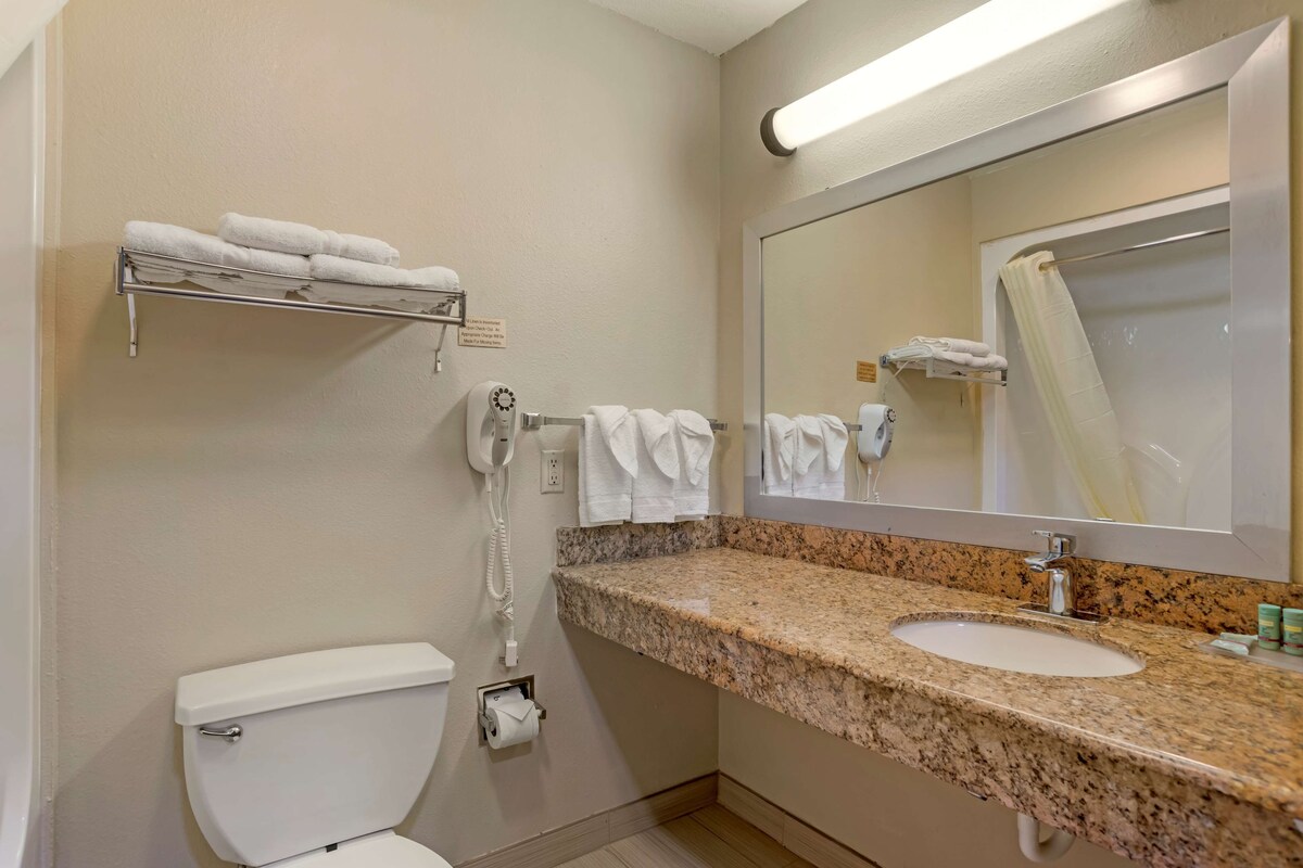 A bathroom with a toilet, a sink, a towel rack, a mirror, and a towel dispenser.