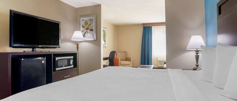 A hotel room with a large bed, a flat-screen TV, a microwave, a desk, and a chair.