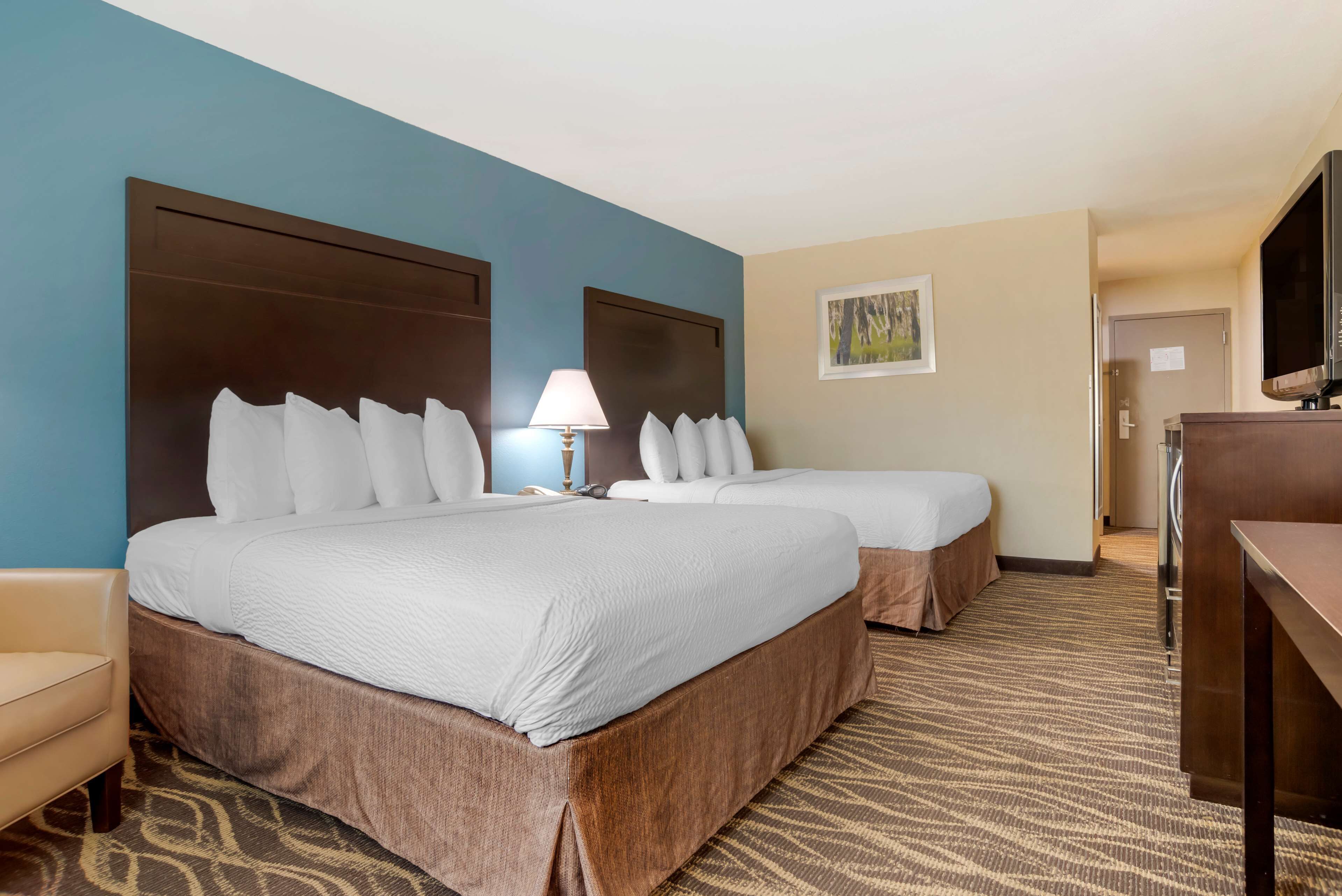 A hotel room with two beds, a desk, a lamp, and a television.
