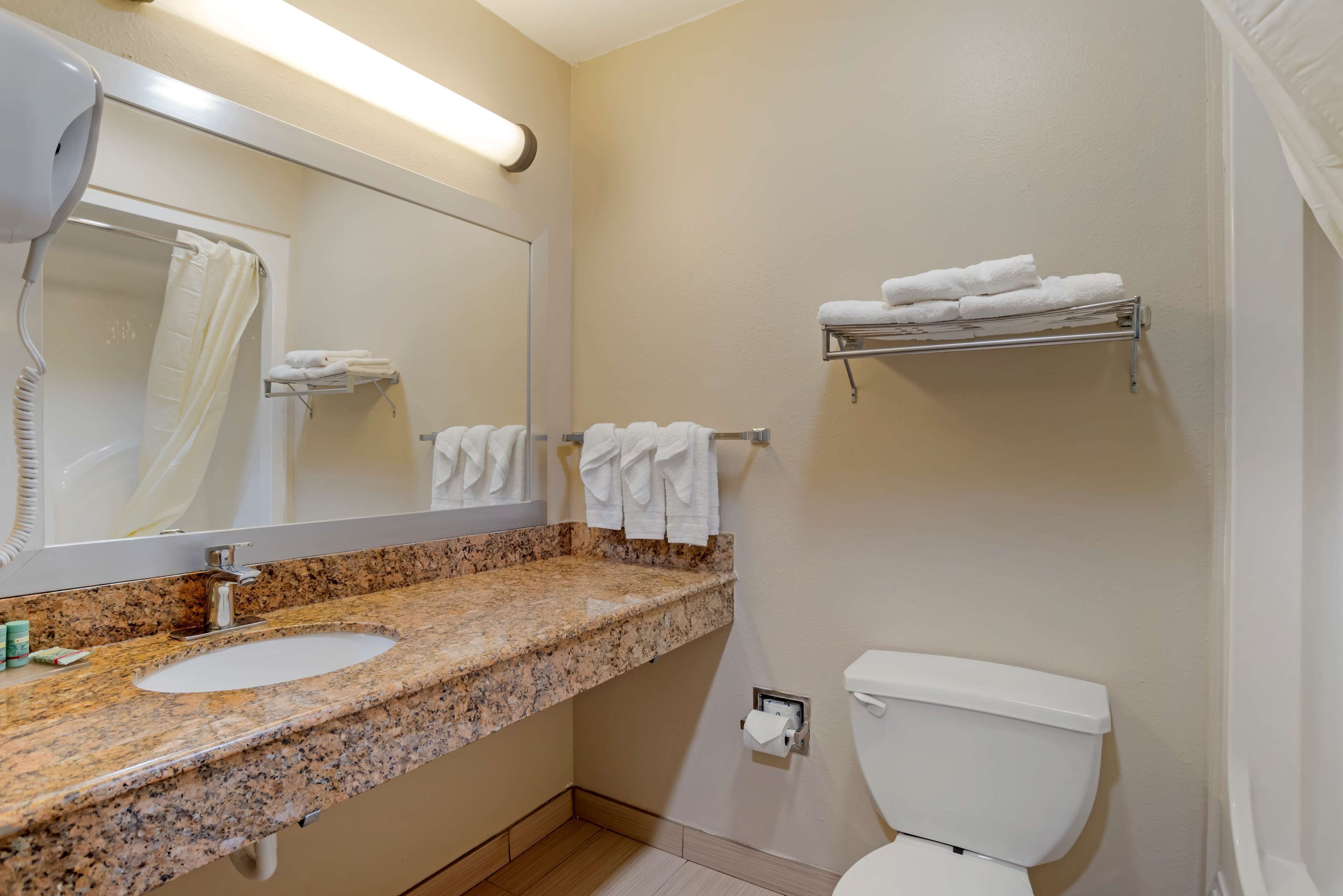 Un baño con lavamanos de granito, un espejo, inodoro y toallero con toallas dobladas.