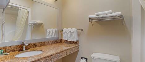 A bathroom with a granite countertop sink, a mirror, a toilet, and a towel rack with folded towels.