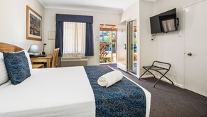 Habitación de hotel con cama, escritorio con lámpara, televisor montado en la pared y vista al balcón exterior.