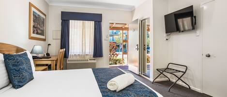 A hotel room with a bed, a desk with a lamp, a TV mounted on the wall, and a view of the outside balcony.