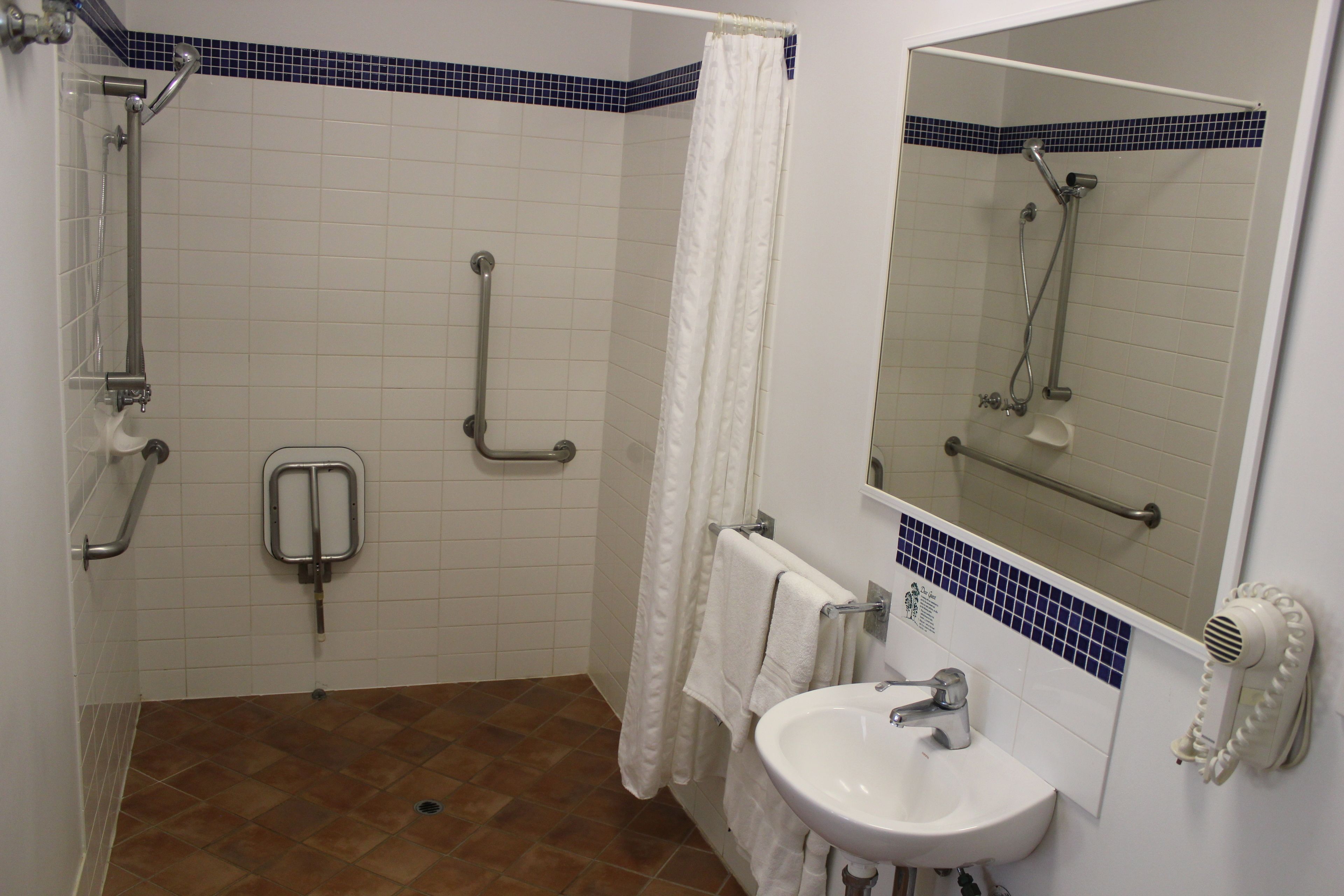 A bathroom with a shower, grab bar, and a sink with a mirror.