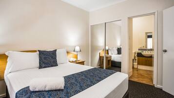 A hotel room with a large bed, a bedside table with a lamp, a wardrobe, and a bathroom visible through an open door.