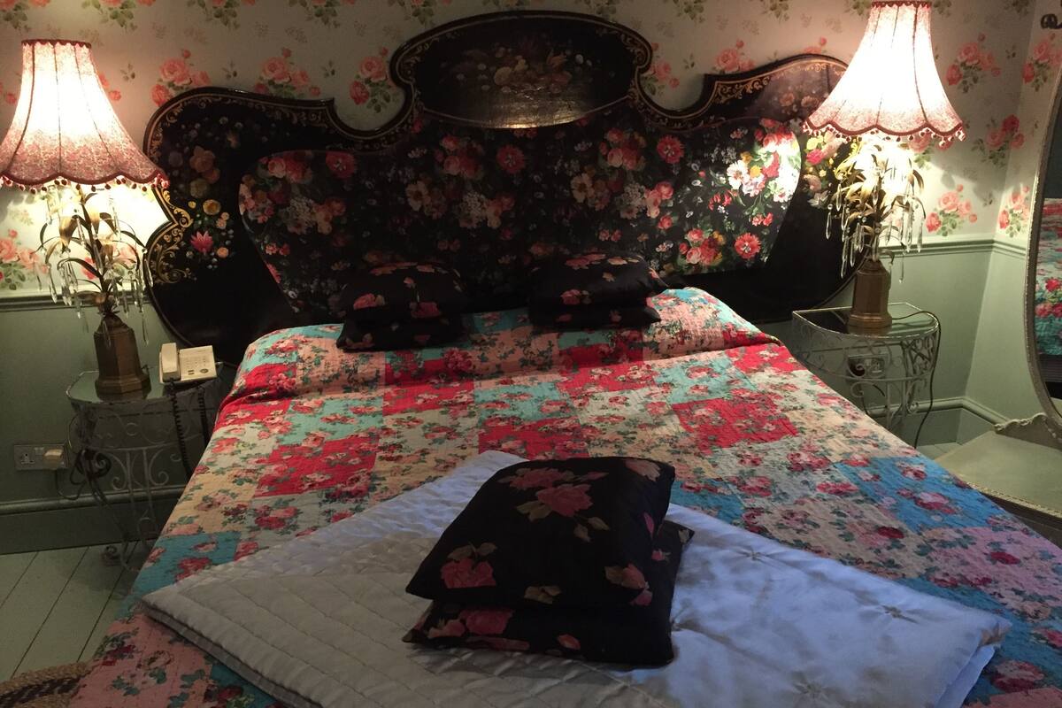 Et soveværelse med et blomstret sengetæppe, en dekorativ sengegavl, to sengeborde med lamper og en telefon ved siden af sengen.