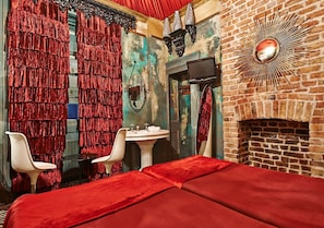 Una habitación con chimenea de ladrillo, un espejo, un televisor y cortinas rojas.