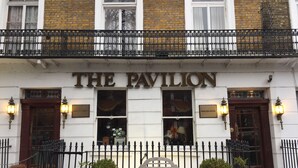 A building with a sign reading "THE PAVILION HOTEL". There are two doors, a bench, and potted plants in front. - The Pavilion Hotel (London)
