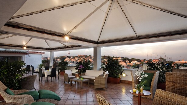 An outdoor patio area with wicker furniture, a round table, and potted plants. - Grand Hotel Tiberio (Rome)