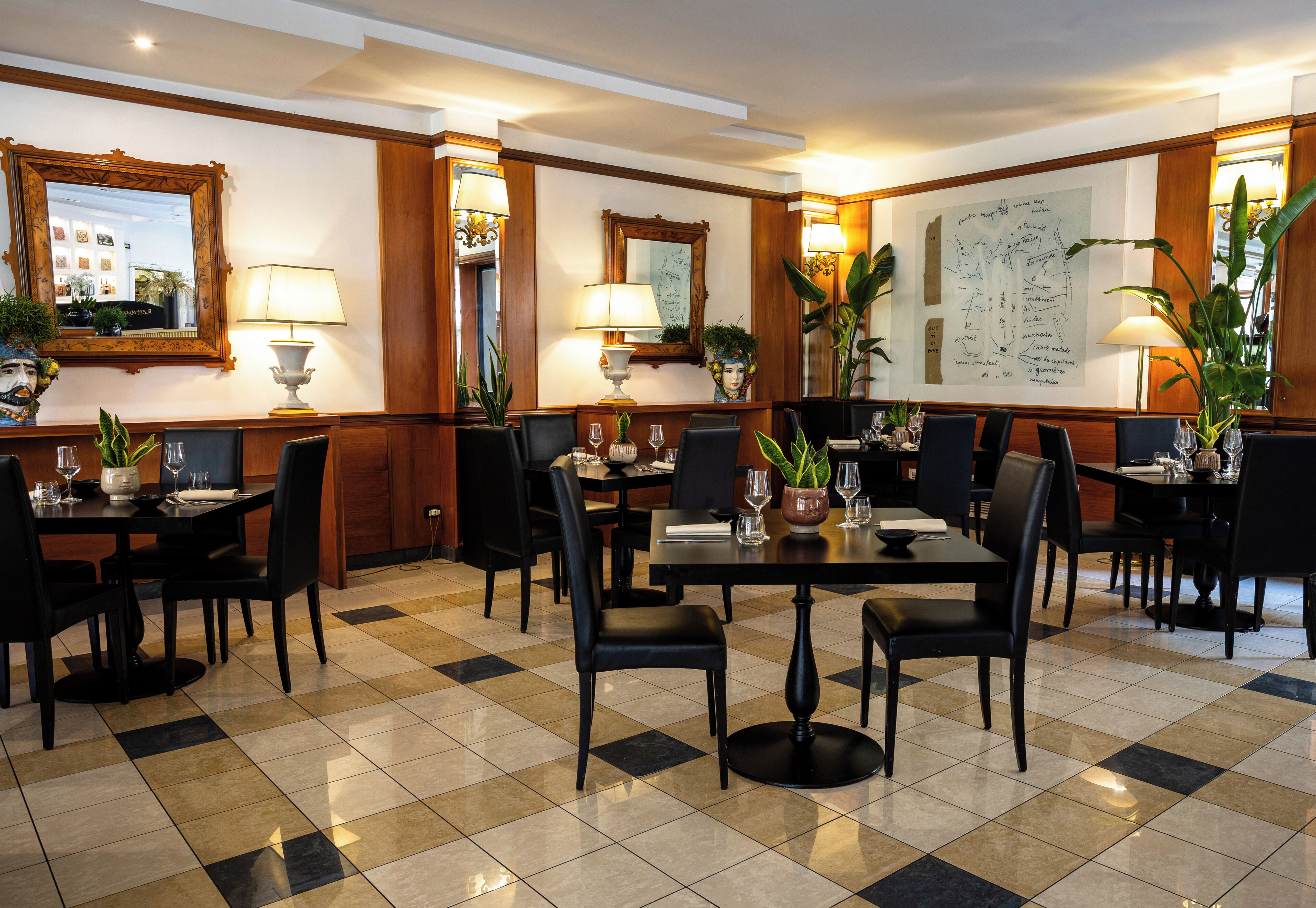Una hall d'albergo con pavimento a scacchi, diversi tavoli da pranzo, sedie e piante in vaso.