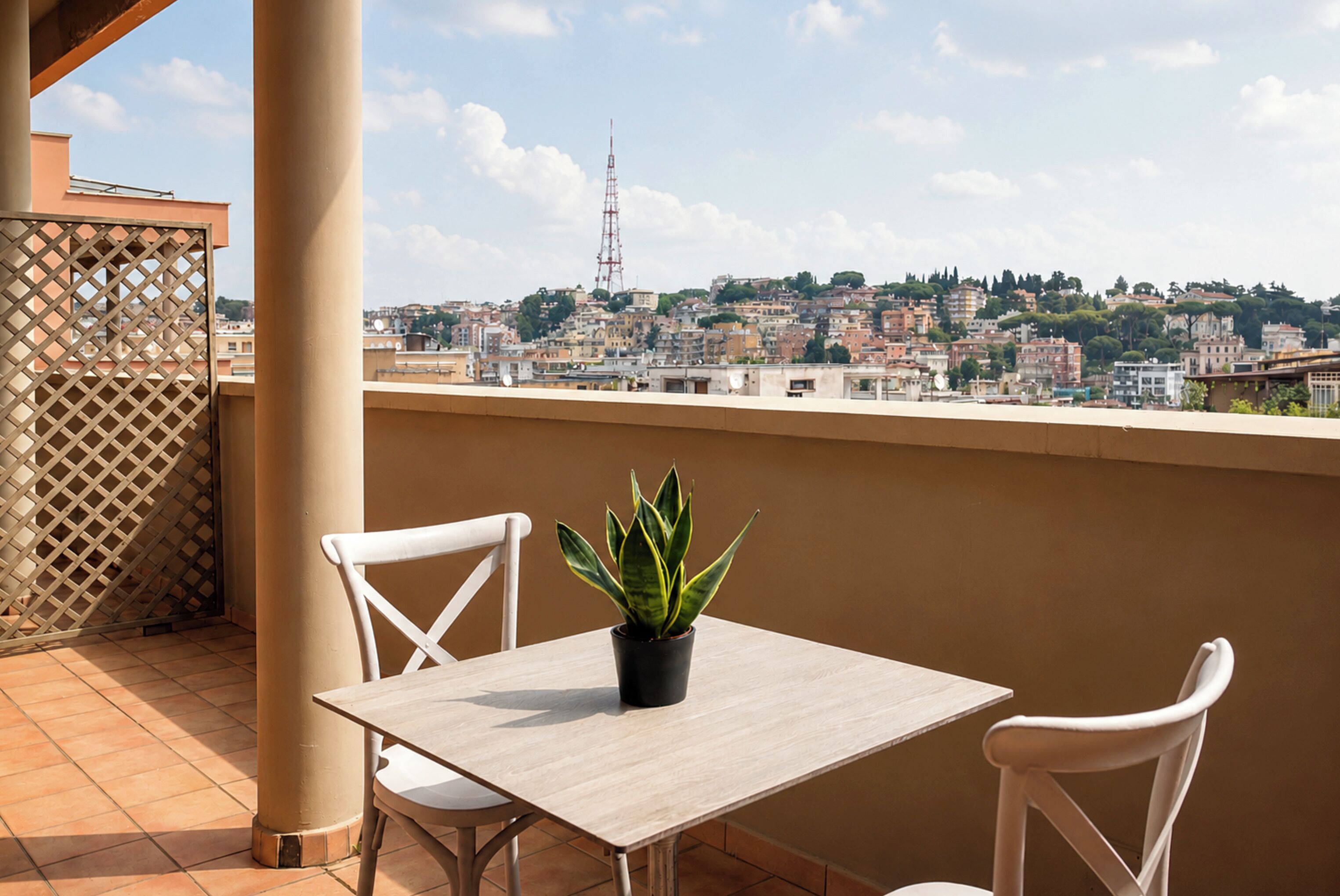 A balcony with a table and chairs, a potted plant, and a view of a cityscape.