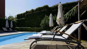 A poolside area with lounge chairs and umbrellas, surrounded by a hedge and a building. - Grand Hotel Tiberio (Rome)