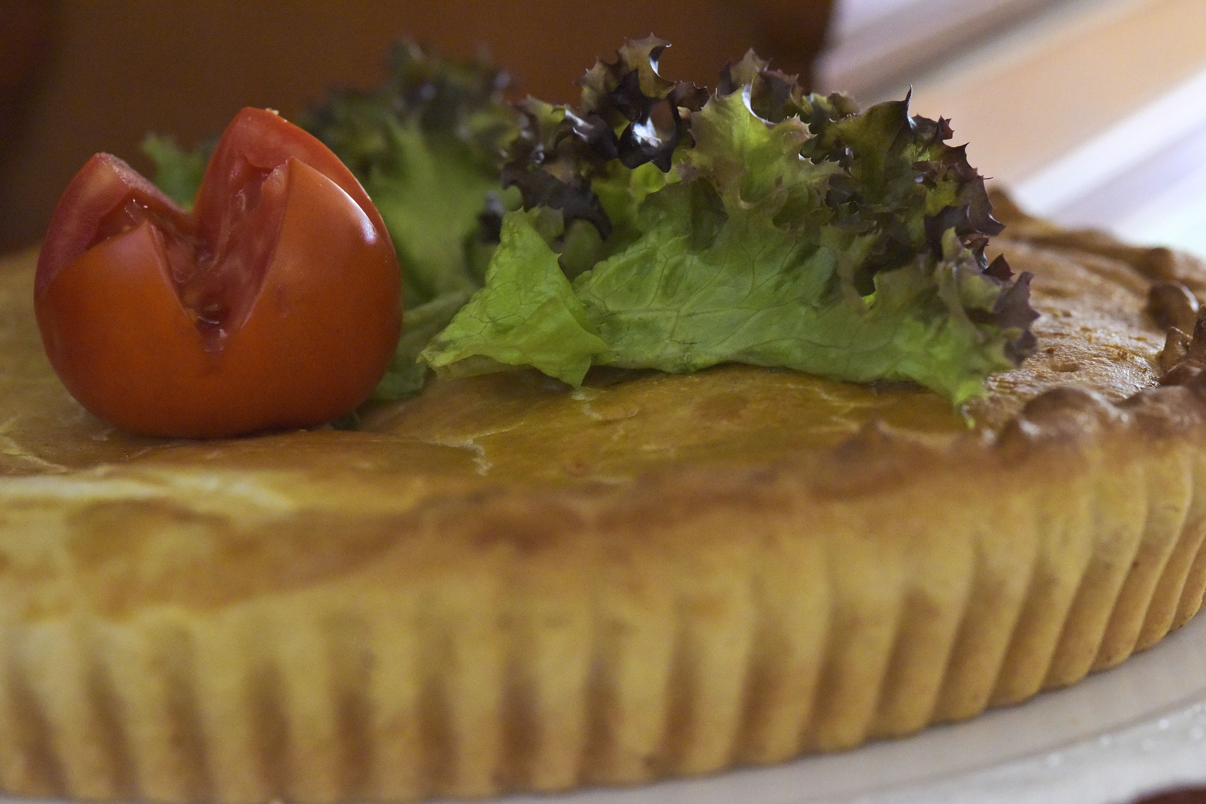 Een ronde quiche met korst, versierd met een tomaat en sla.