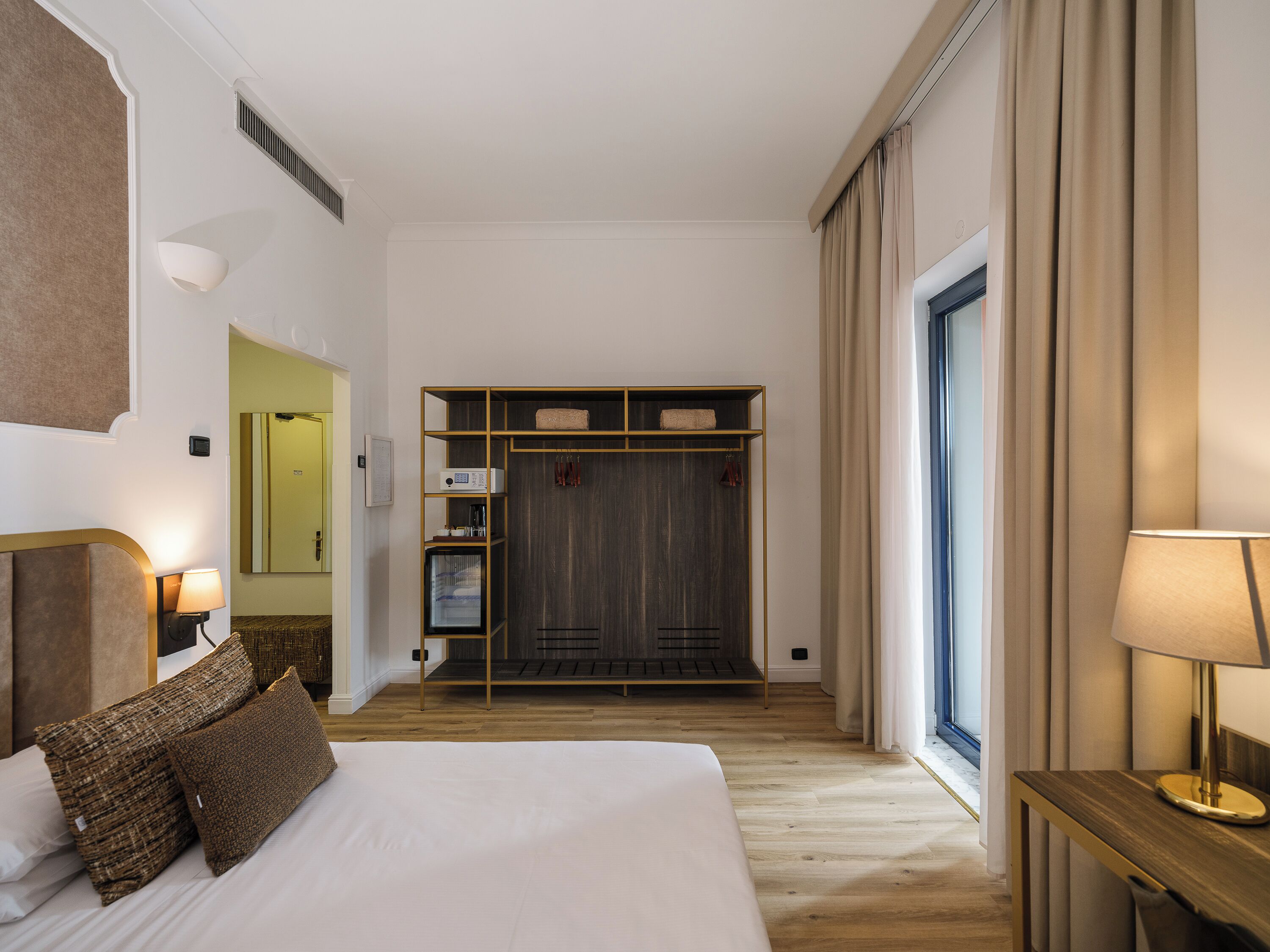 Une chambre d’hôtel avec un lit, des lampes de chevet, une armoire, un miroir et une fenêtre avec des rideaux.