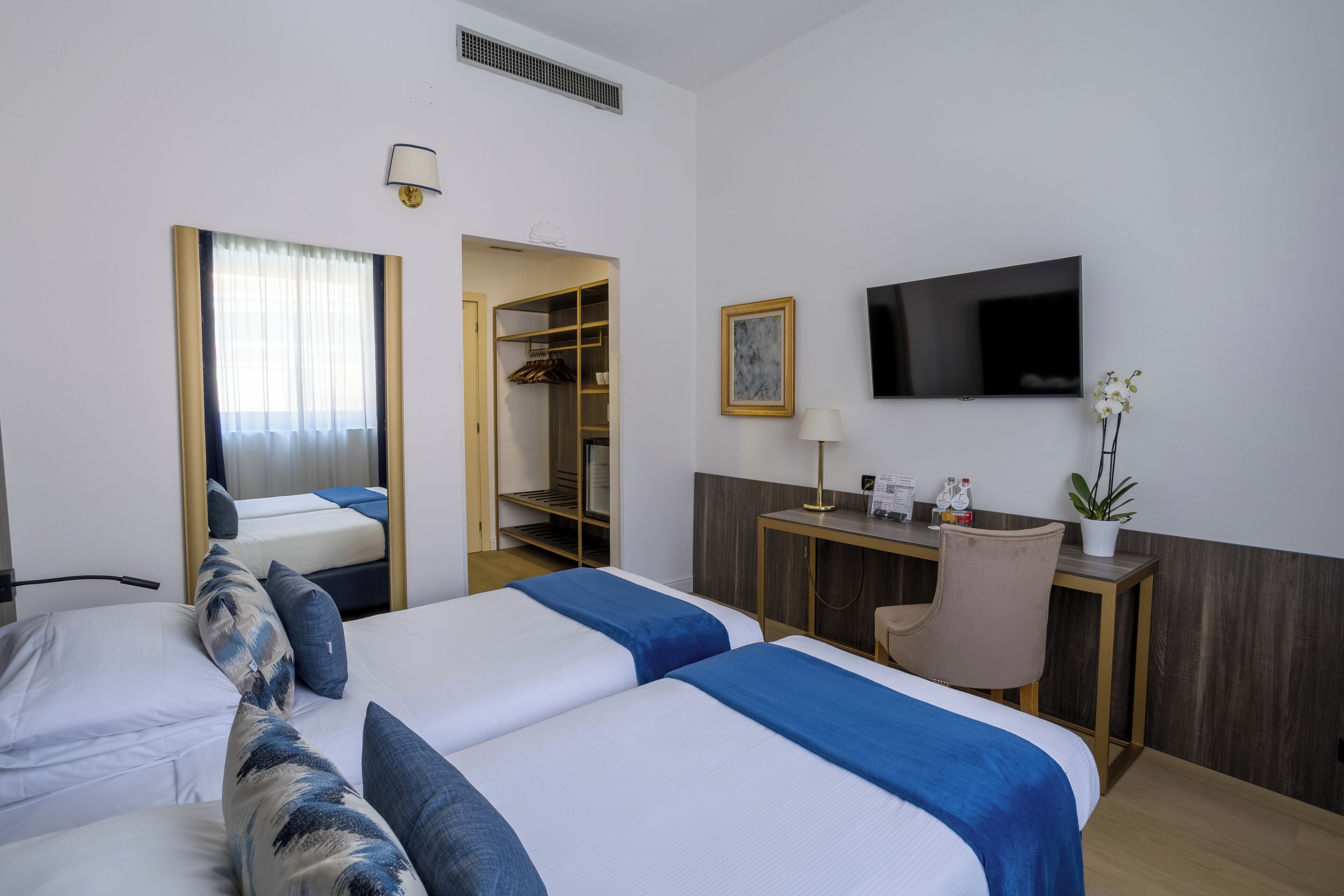 Una camera d'albergo con due letti, una scrivania, una sedia, una TV e un armadio.