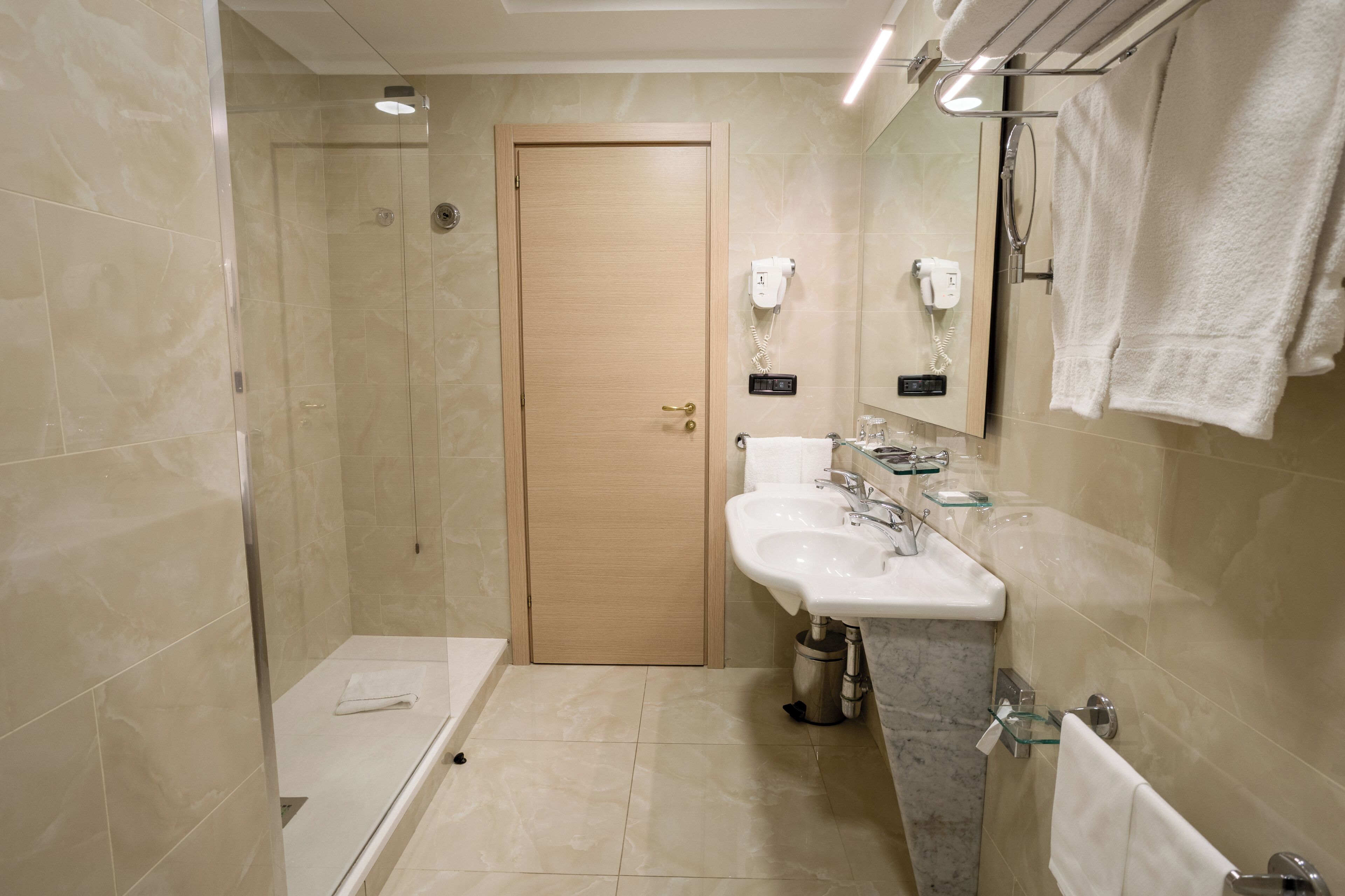 A modern bathroom with a glass shower enclosure, a wooden door, a white sink with a marble countertop, and a glass-topped vanity.