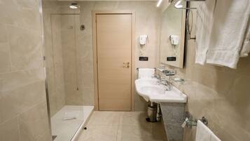 A modern bathroom with a glass shower enclosure, a wooden door, a white sink with a marble countertop, and a glass-topped vanity.