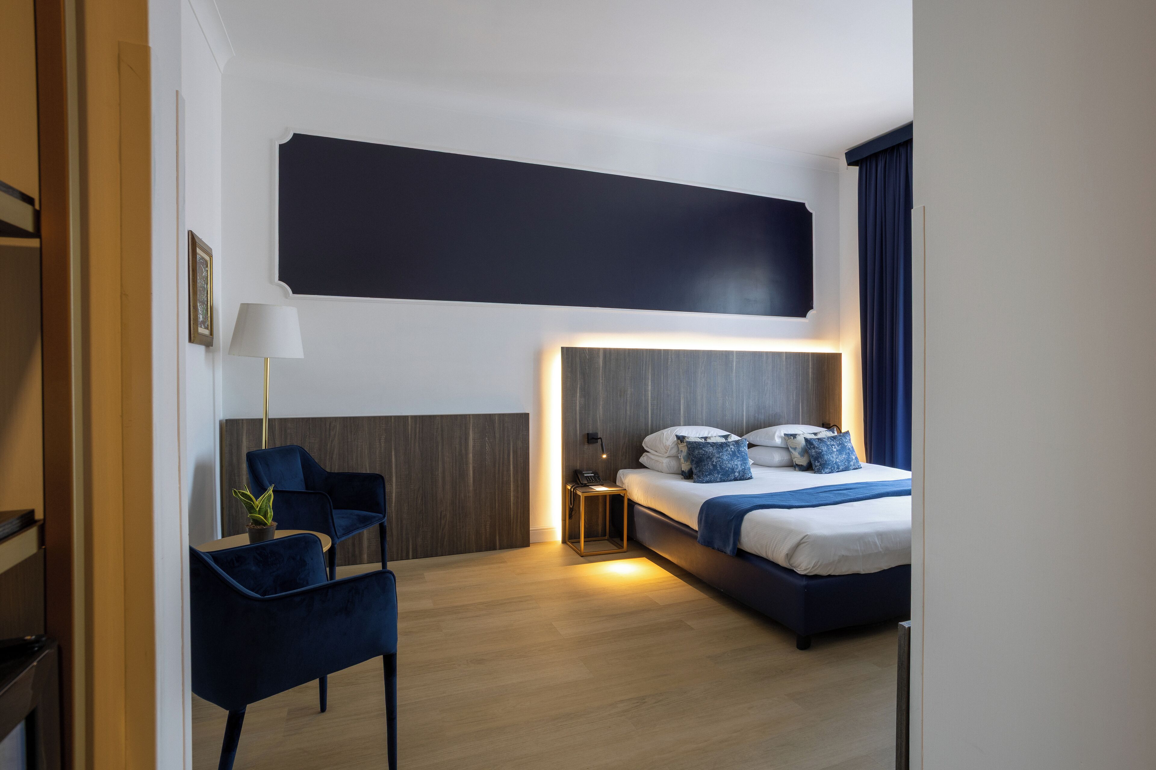 A modern hotel room with a bed, bedside table, lamp, and a chair.