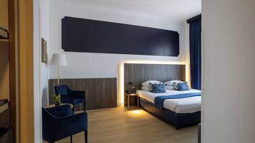 A modern hotel room with a bed, bedside table, lamp, and a chair.