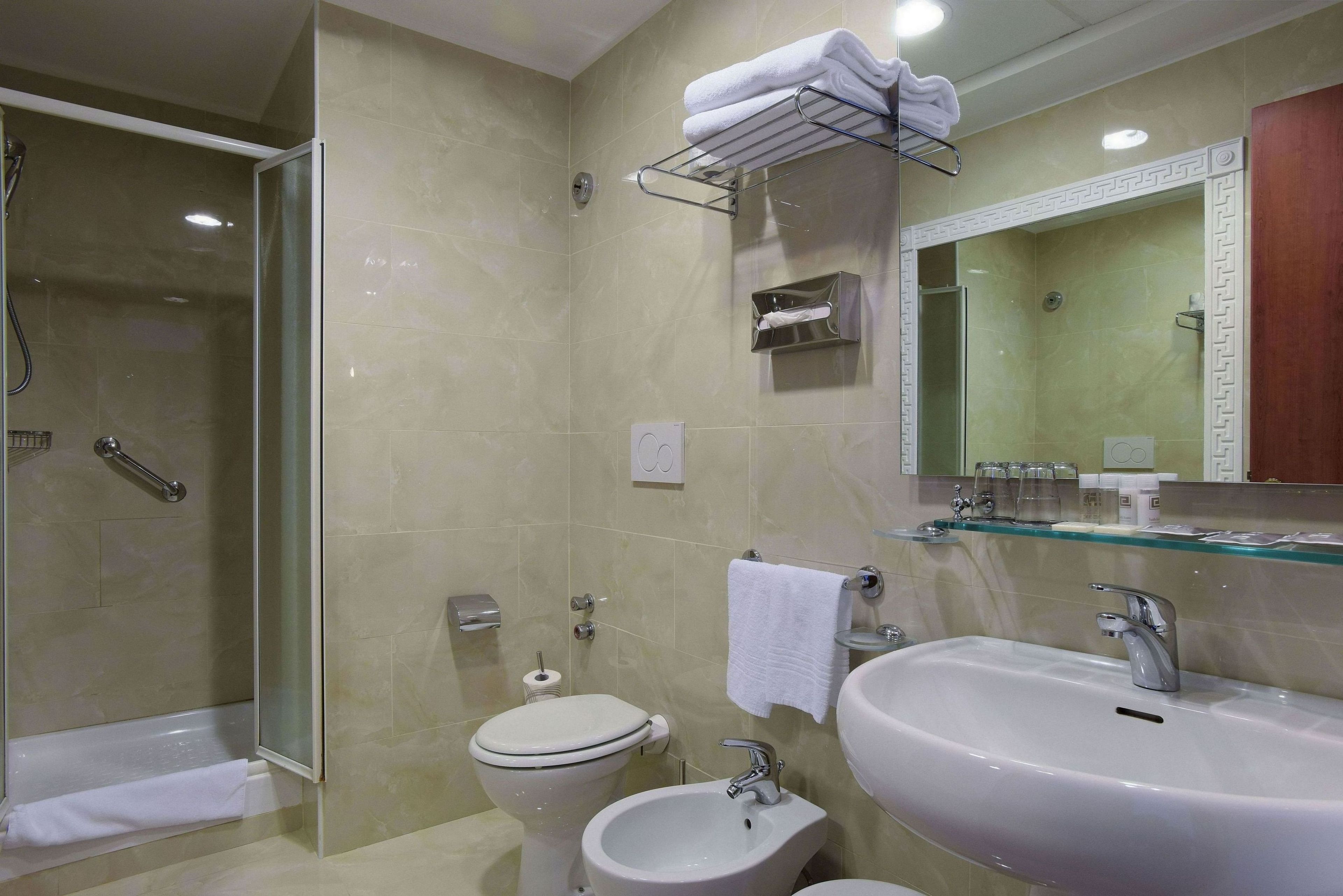 A modern bathroom with a glass-enclosed shower, a toilet, a bidet, and a sink with a mirror above.