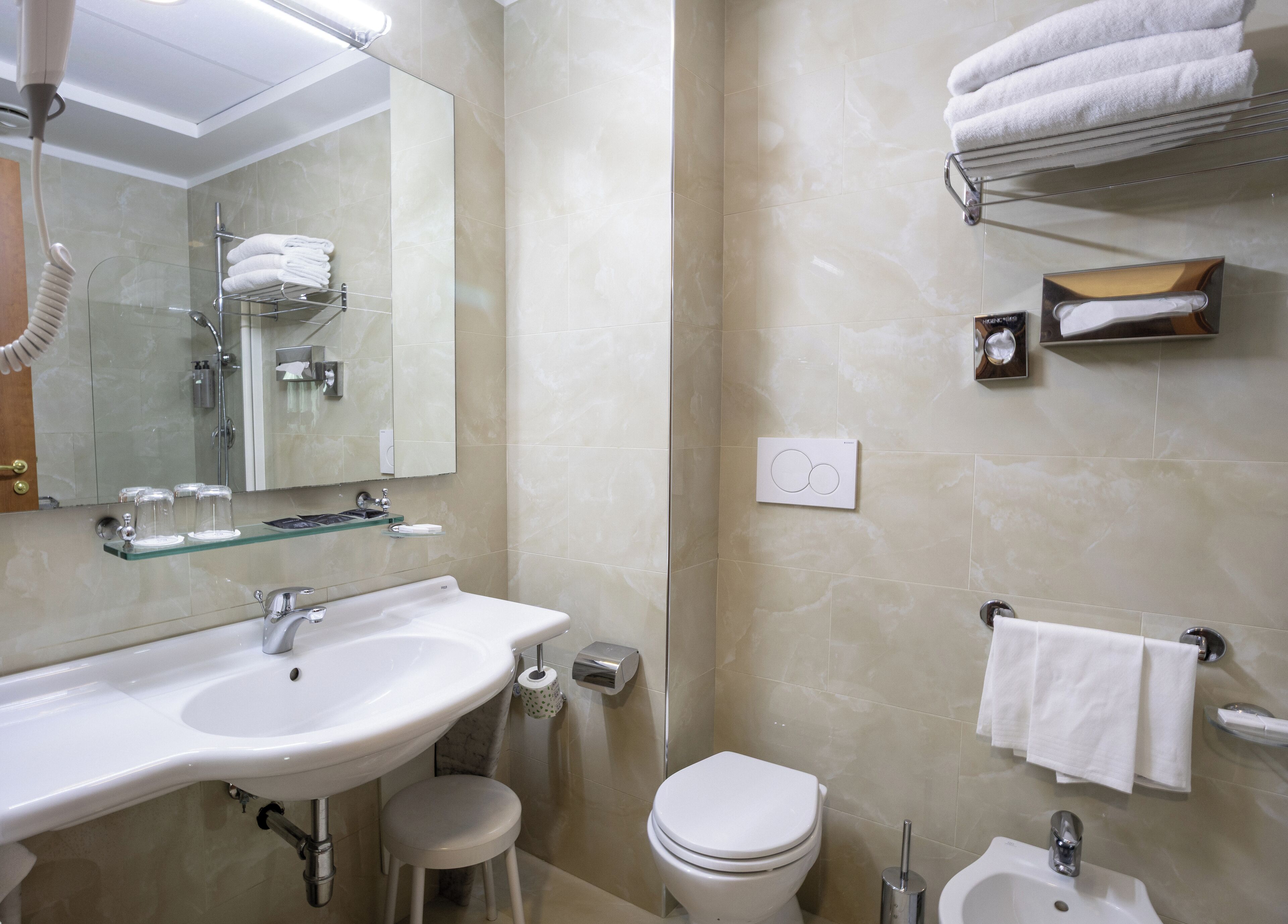 A modern bathroom with a large sink, toilet, and bidet. There are towels and toiletries visible.