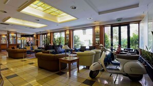 A spacious lobby with a checkered floor, comfortable seating, a scooter, and large windows offering a view of the outdoors. - Grand Hotel Tiberio (Rome)