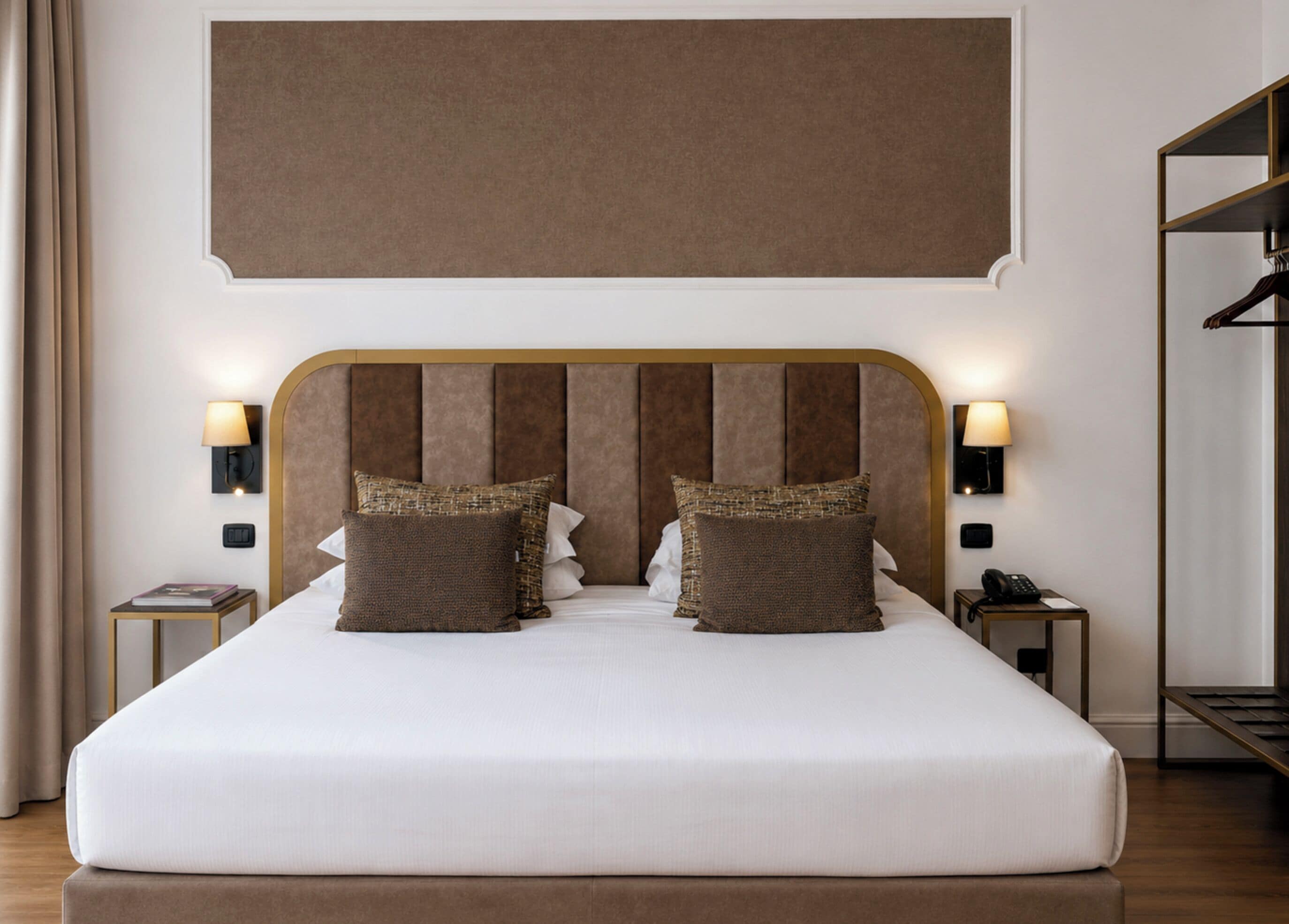 Una cama grande con cabecera de madera, dos mesitas de noche con lámparas y una pantalla grande montada en la pared sobre la cama.