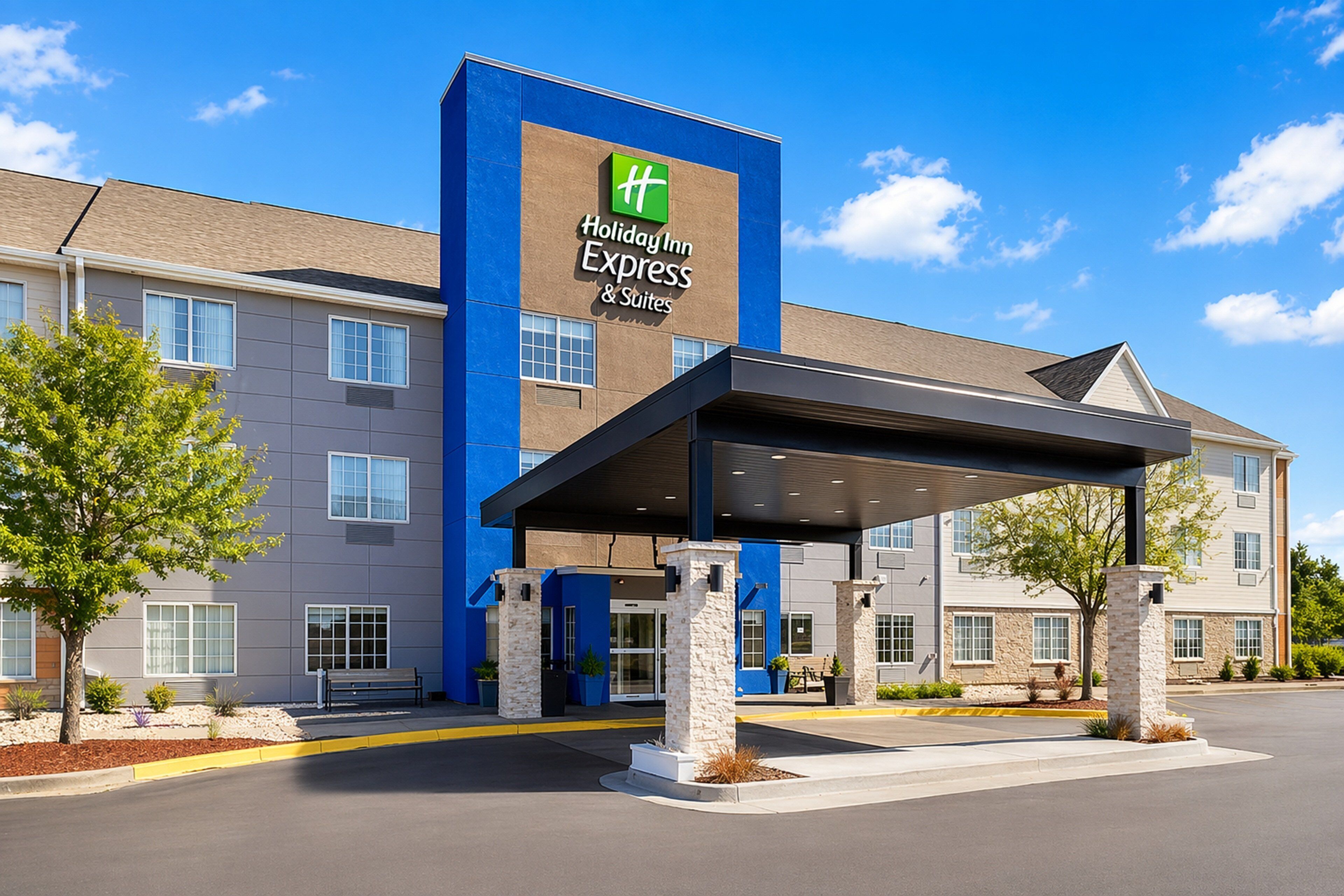 A Holiday Inn Express & Suites building with a blue and beige exterior, a covered entrance, and a clear sky.