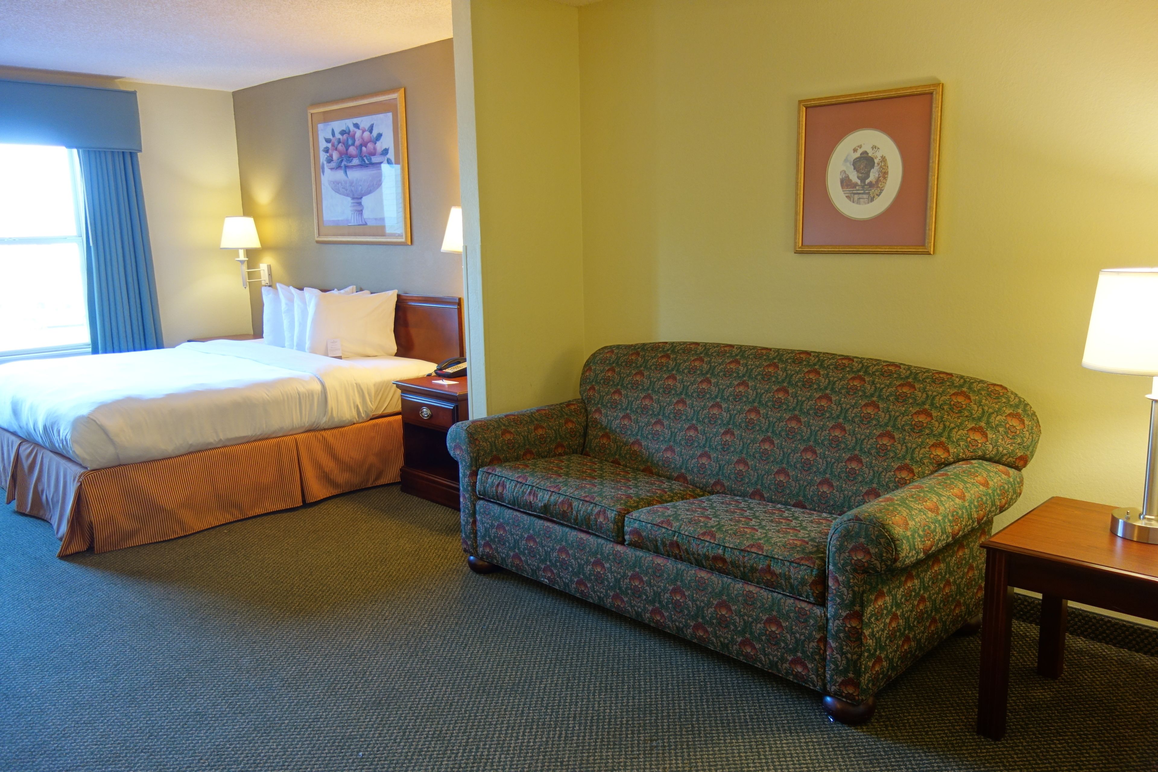A hotel room with a bed, a sofa, a nightstand, and two wall-mounted lamps.