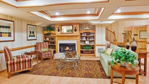 A spacious living room with a fireplace, striped armchairs, a coffee table, and a bookshelf. - Country Inn & Suites by Radisson, McDonough, GA (McDonough)
