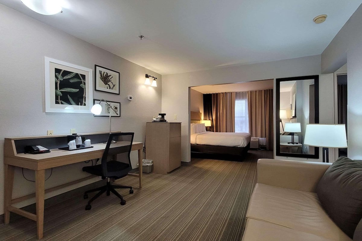 A hotel room with a desk, chair, bed, and a small couch.