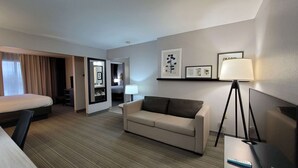A hotel room with a bed, a sofa, a desk, a lamp, and framed artwork on the wall. - Country Inn & Suites by Radisson, McDonough, GA (McDonough)