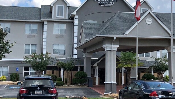 A Country Inn & Suites building with a two-story structure, a covered entrance, and a flag. - Country Inn & Suites by Radisson, McDonough, GA (McDonough)