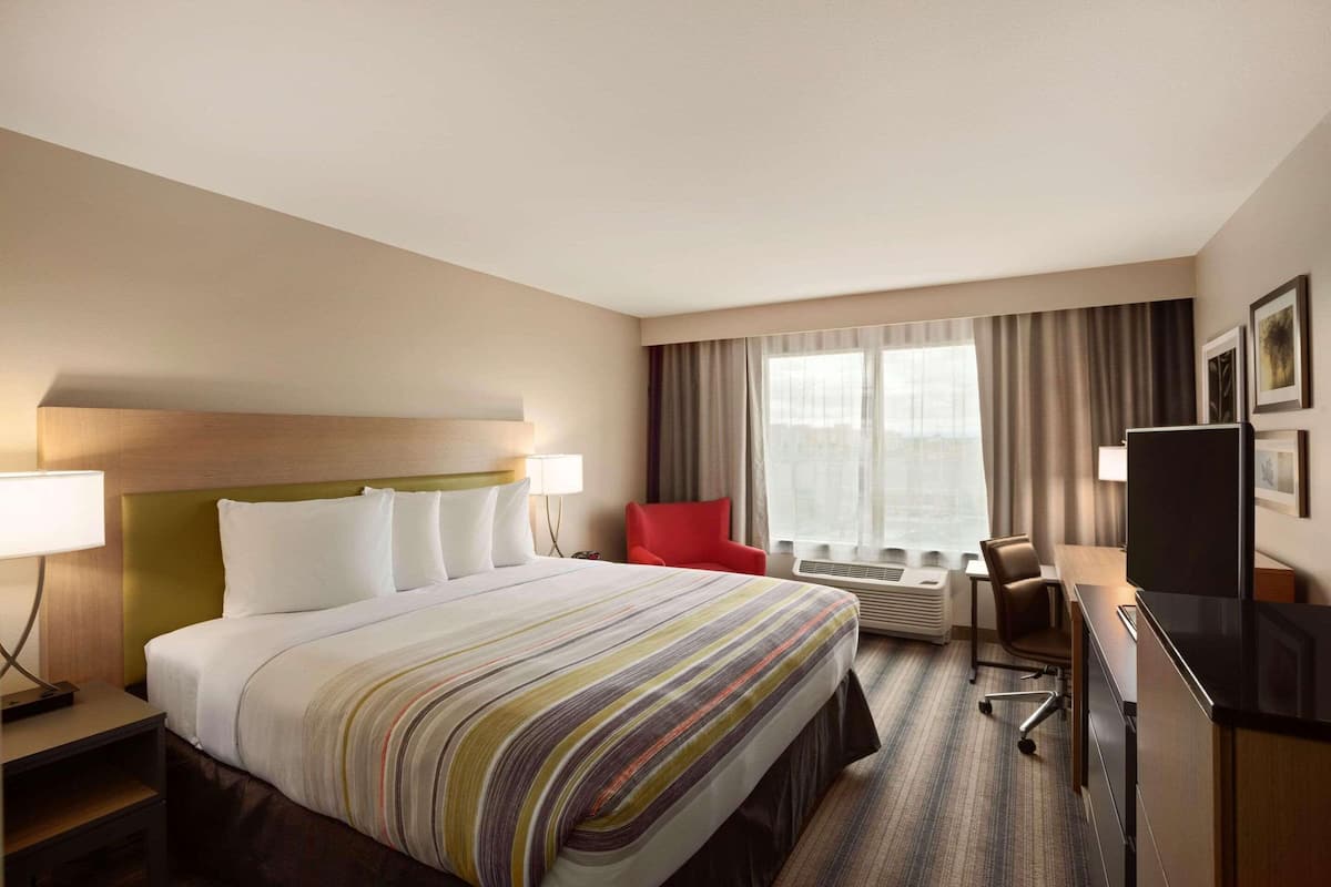 A hotel room with a large bed, a desk with a chair, a TV, and a window with curtains.
