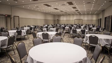 A large conference room with multiple round tables and chairs, carpeted flooring, and a high ceiling with recessed lighting.