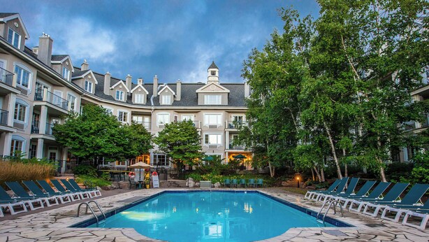 A swimming pool with lounge chairs, surrounded by stone tiles, and a building with multiple balconies in the background. - Holiday Inn Express and Suites Tremblant by IHG (Mont-Tremblant)