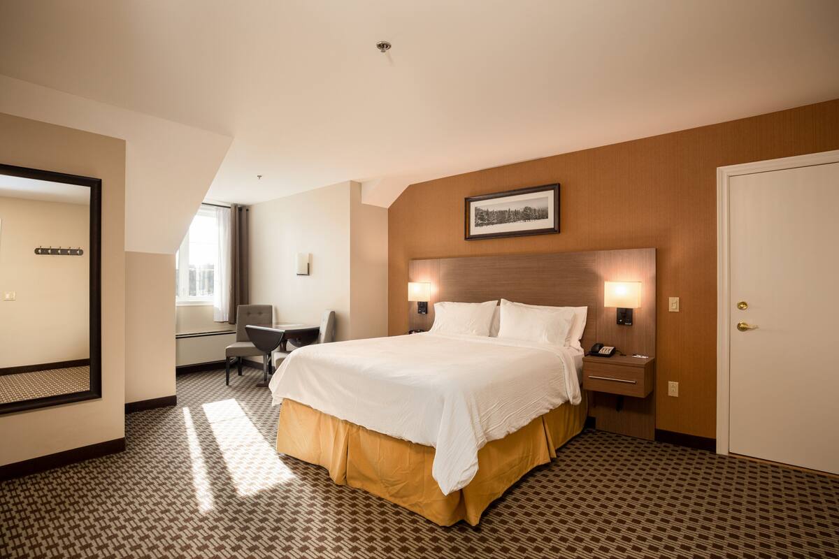 Ein Hotelzimmer mit einem großen Bett, einem Schreibtisch, einem Stuhl, einem Spiegel und einer Tür.