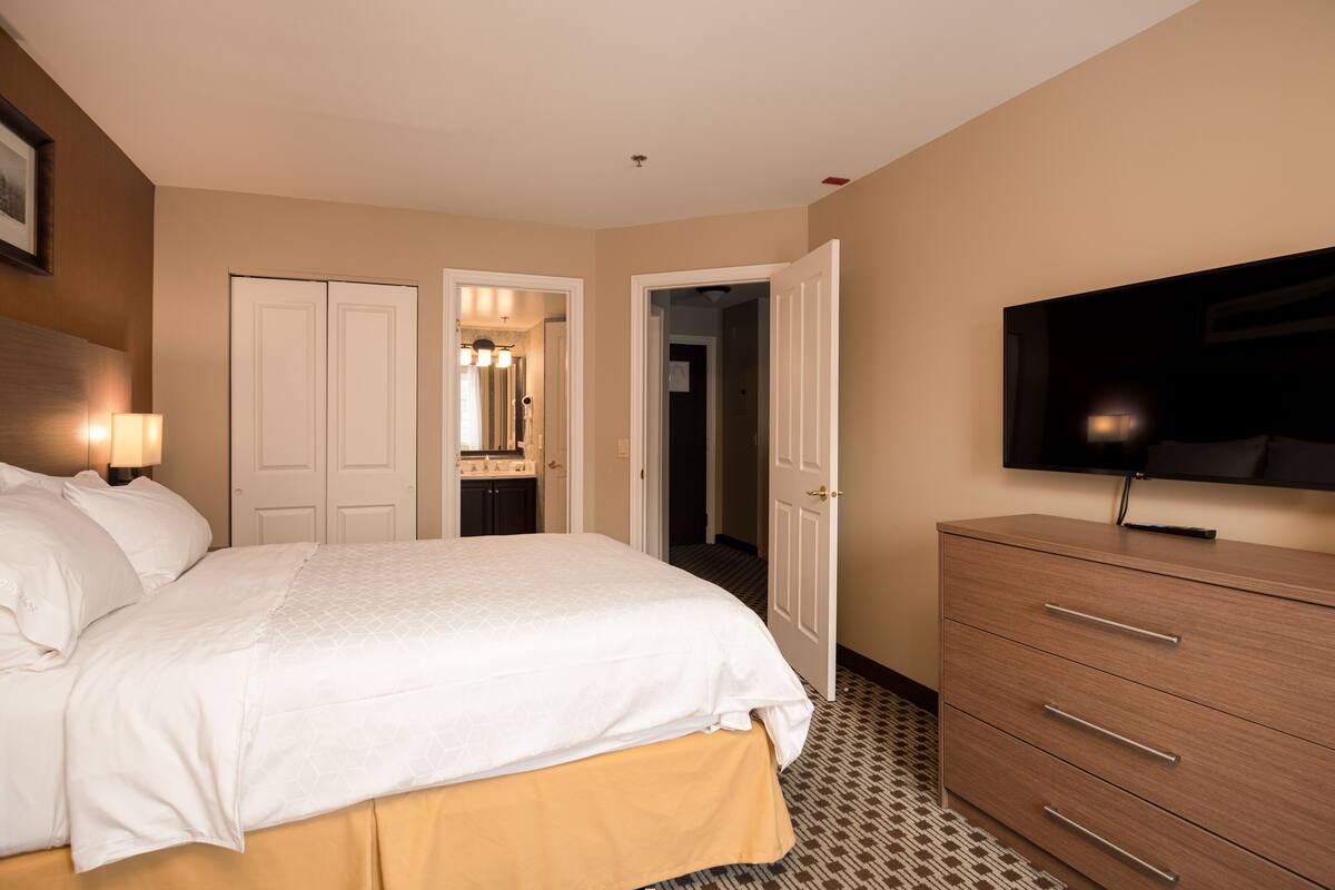 Ein Hotelzimmer mit Bett, Schminktisch, Fernseher und einem durch eine offene Tür einsehbaren Badezimmer.