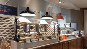A buffet setup with multiple food stations, overhead lighting, and a tiled backsplash. - Holiday Inn Express and Suites Tremblant by IHG (Mont-Tremblant)