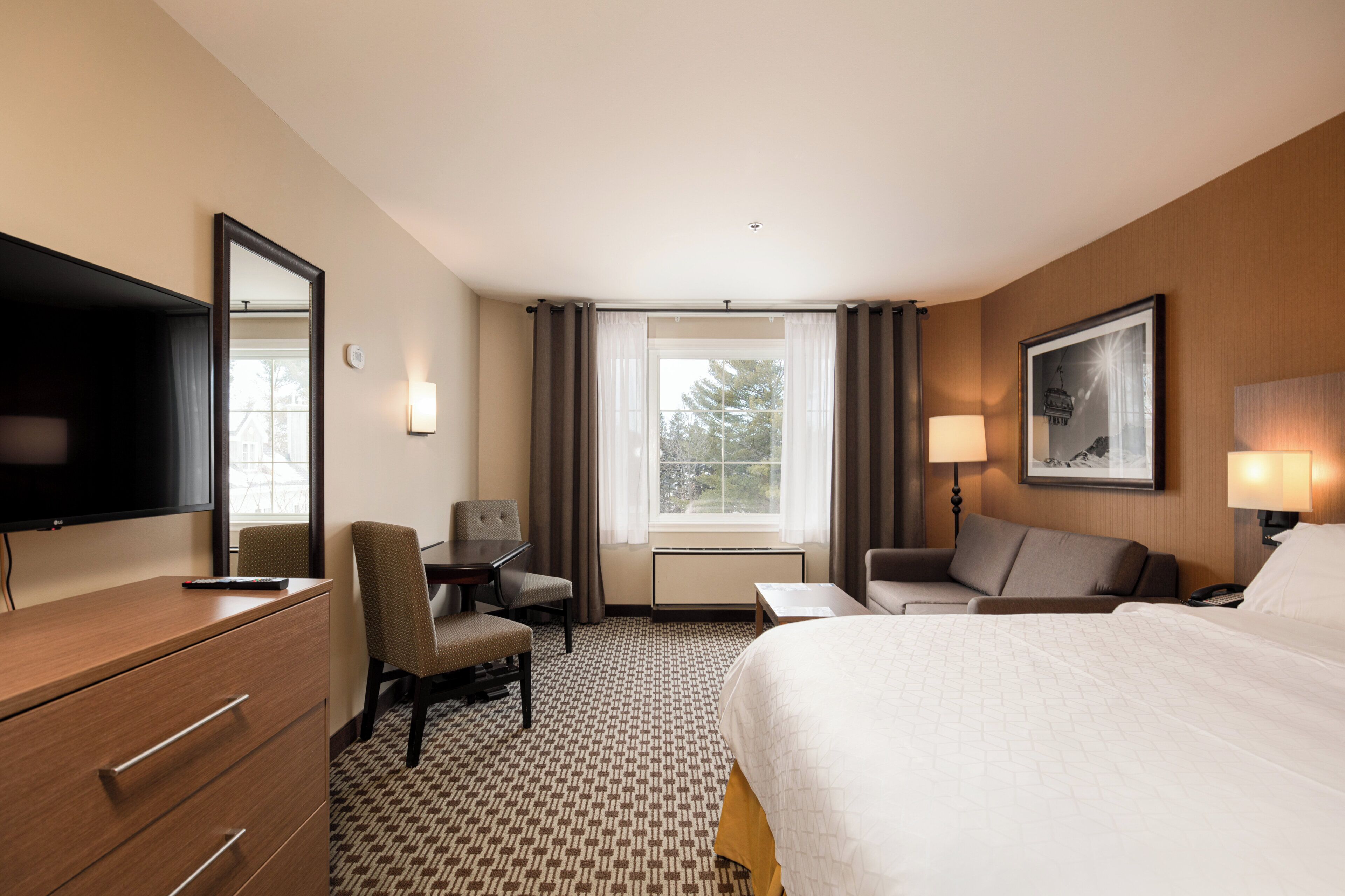 A hotel room with a bed, a desk, a chair, a television, and a window with curtains.