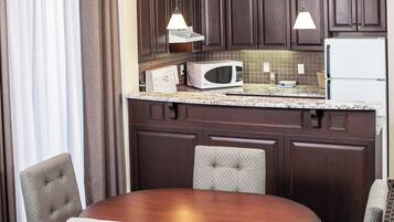 A compact kitchen with dark wood cabinets, a microwave, a refrigerator, and a dining area with a table and chairs.