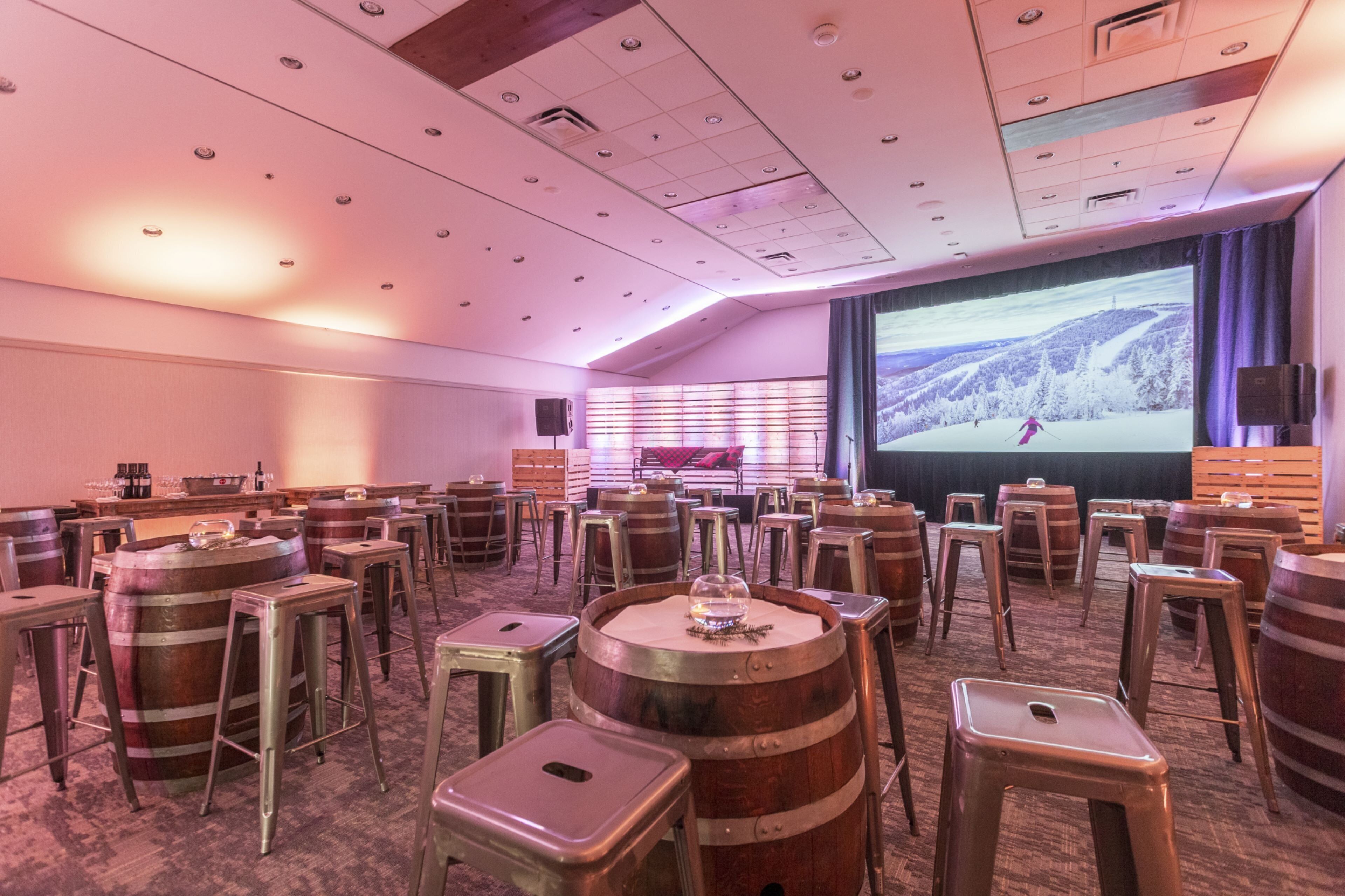 A conference room with multiple wooden barrels, stools, and a large screen displaying a snowy landscape.