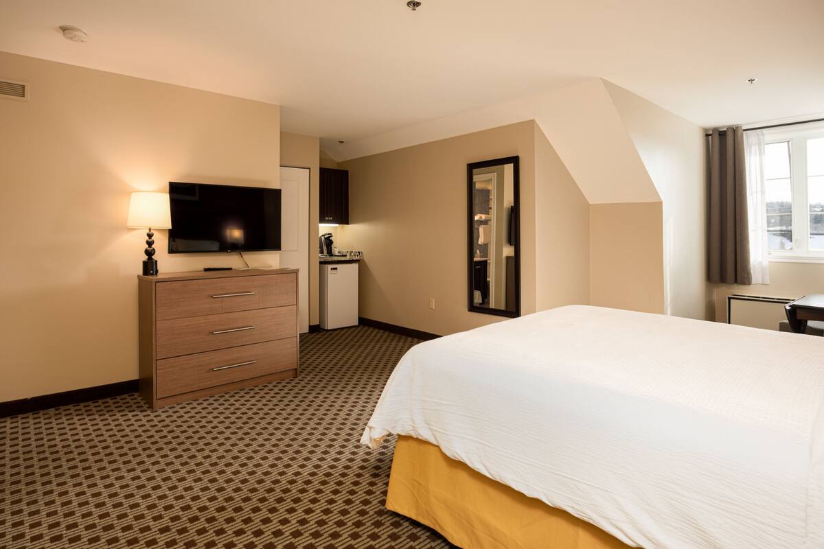 Ein Hotelzimmer mit Bett, Kommode, Fernseher, Schreibtisch und einem Fenster mit Vorhängen.